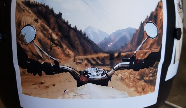Airbrushed Painting of a Touring Helmet with image of motorbike handle bars on a scenic road paintied like a poleroid photo Close up with mountains on each side